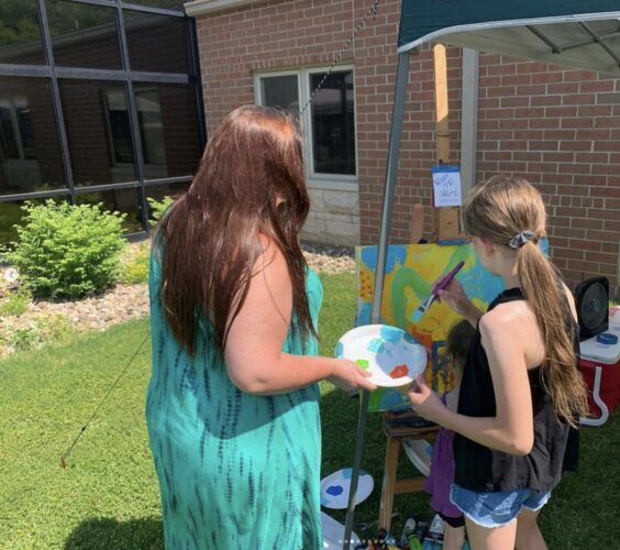 ARTIST Mindy Yarbrough Langford, left, helps a girl with a collaborative painting.